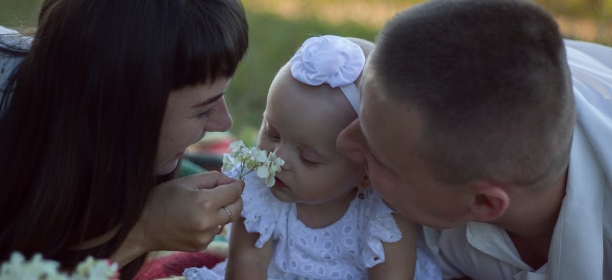 A loving family moment with parents and baby at a sunny outdoor picnic.