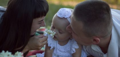A loving family moment with parents and baby at a sunny outdoor picnic.