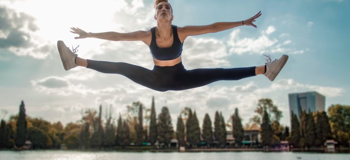 Dynamic shot of a woman in activewear leaping by a lakeside, capturing energy and freedom.