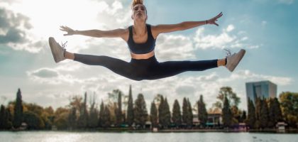Dynamic shot of a woman in activewear leaping by a lakeside, capturing energy and freedom.