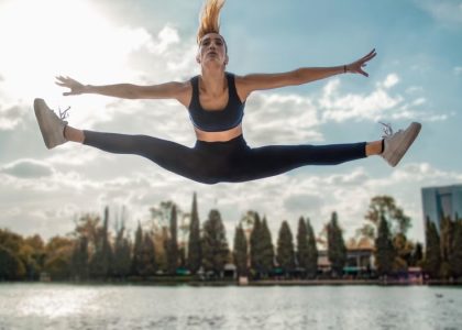 Dynamic shot of a woman in activewear leaping by a lakeside, capturing energy and freedom.